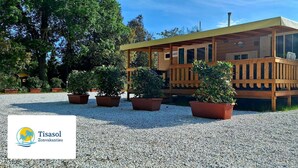 Une cabane en bois dotée d’un porche couvert, entourée de gravier et de plantes en pot.