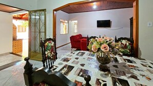 Un área de comedor con una mesa cubierta por un mantel estampado con periódico, un jarrón de flores y un sofá rojo al fondo.