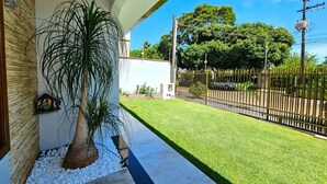 Un espacio exterior cuidado con un sendero de hormigón, una planta grande en maceta, un césped bien arreglado y una valla de metal negro.