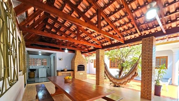 Un patio amplio con una mesa y bancos de madera, una chimenea de ladrillo y una hamaca.