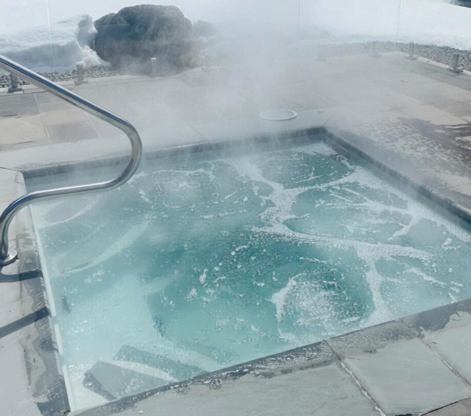 A hot tub with a metal railing, surrounded by a stone or concrete deck.