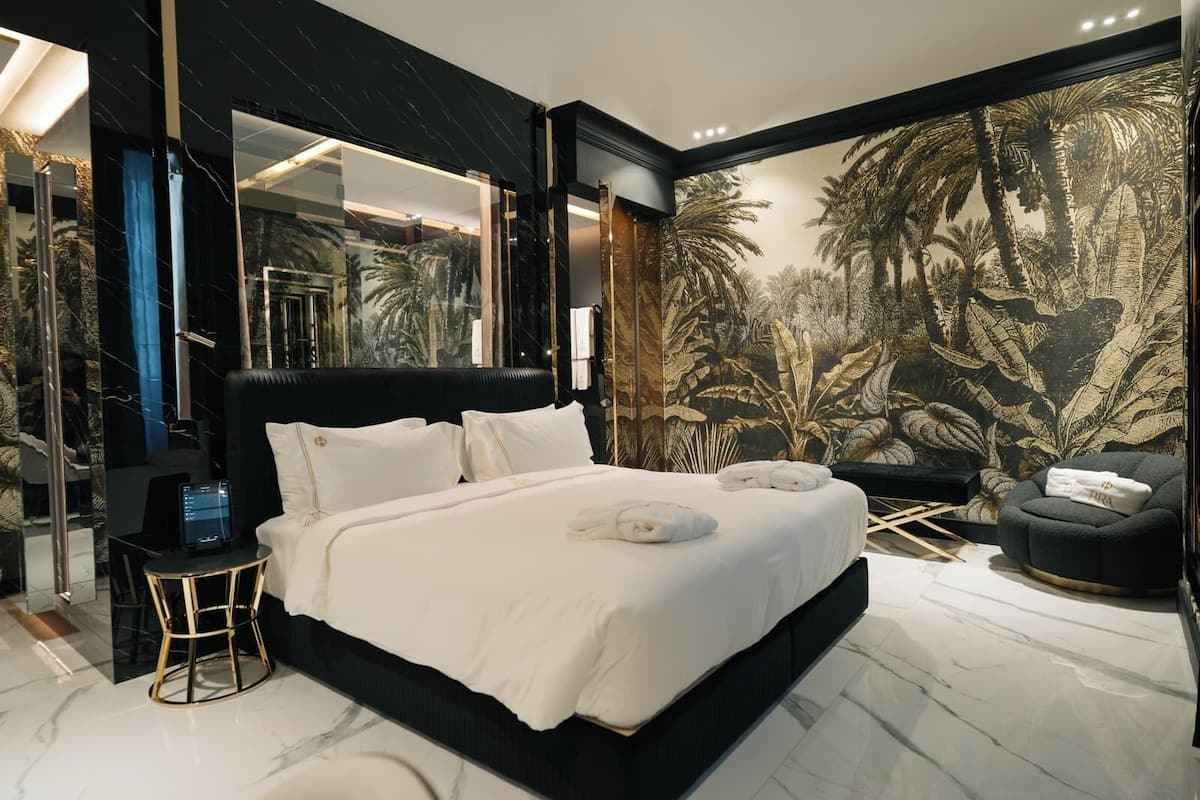 Un dormitorio moderno con una cama grande, una mesita de noche, una silla y un mural con follaje tropical.