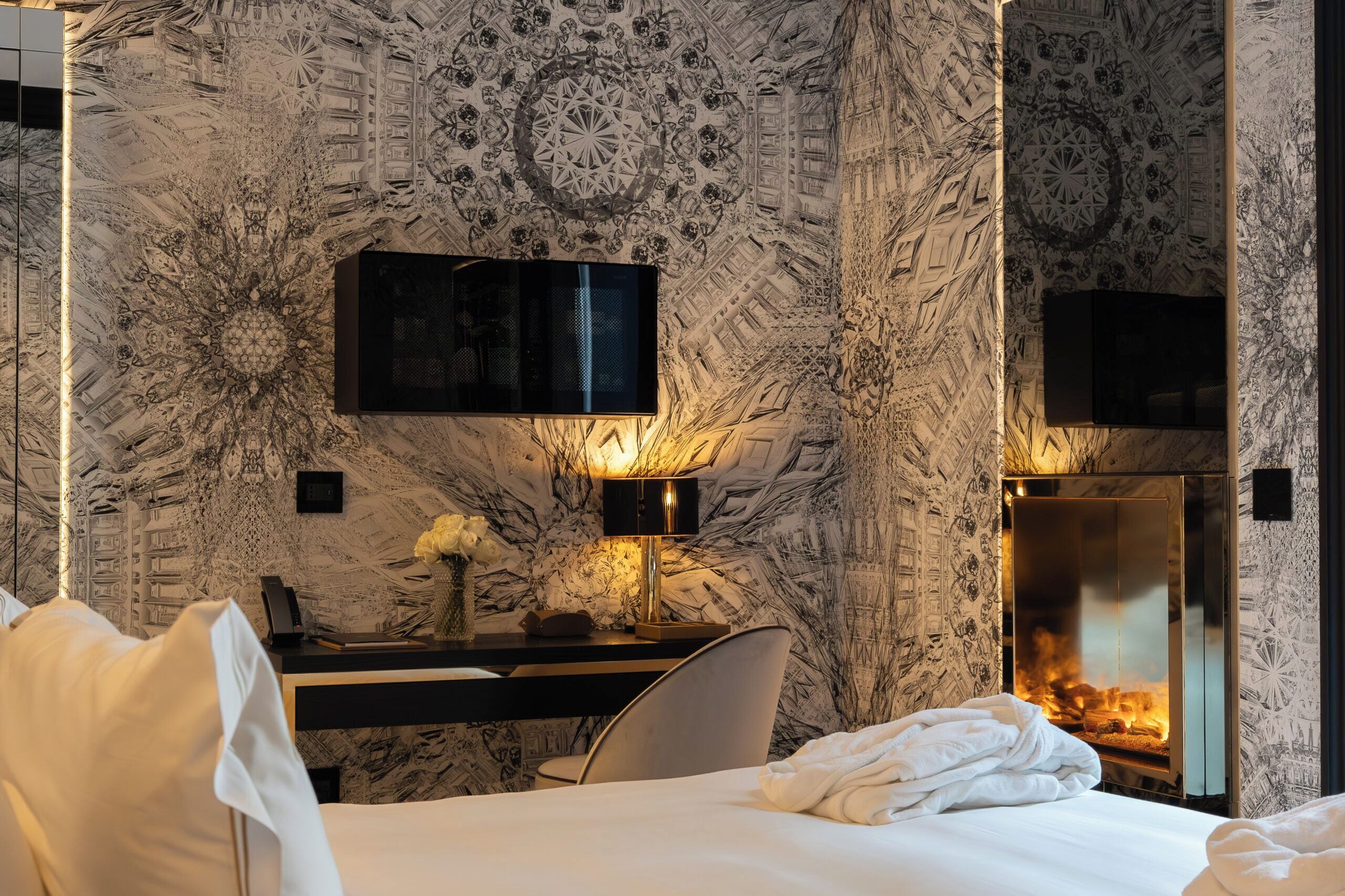 Una camera d'albergo con parete decorata a marmo, una scrivania con lampada, una televisione, un camino e un letto.