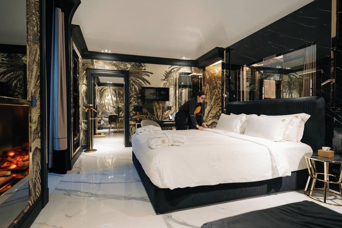 Una habitación de hotel moderna con una cama grande, un televisor y un comedor visible a través de una puerta abierta.