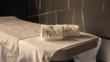 A neatly made bed with a white bedspread and two towels with 'BRA' embroidered on them.