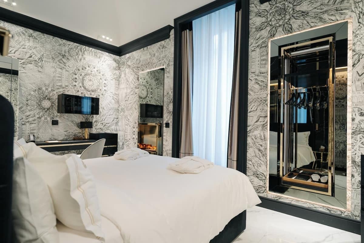 Un dormitorio moderno con una cama grande, televisión, chimenea y un espejo con armario.