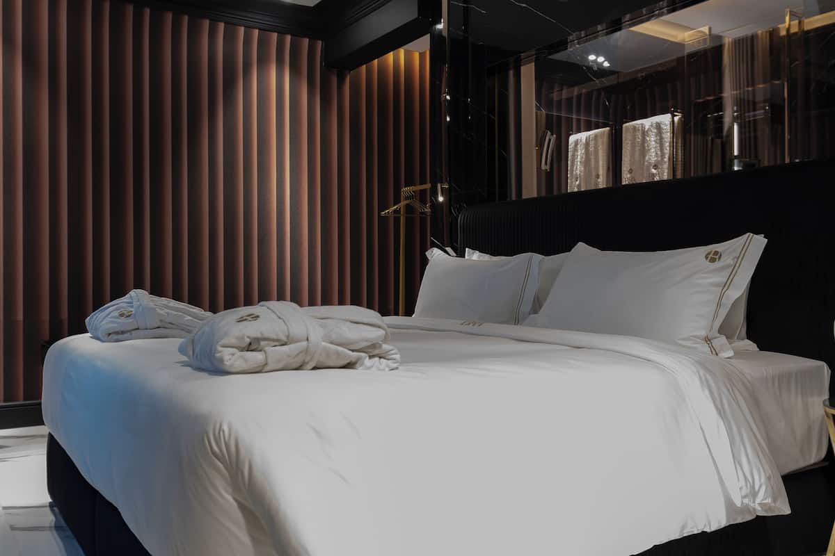Habitación de hotel moderna con una cama grande, paneles de madera oscura y vistas de la ciudad a través de un ventanal.