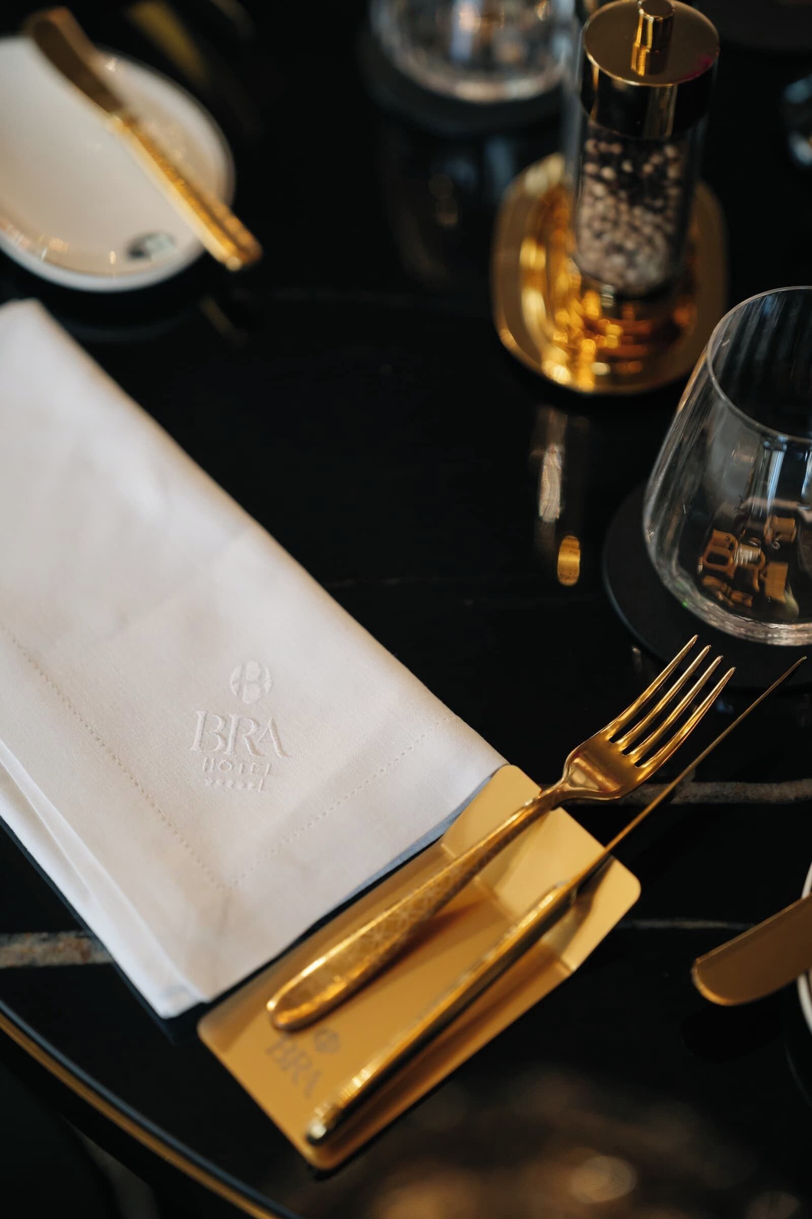 Una mesa dispuesta con servilleta blanca, cubiertos dorados y un candelabro de vidrio.