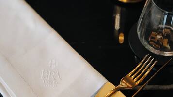 Una mesa dispuesta con servilleta blanca, cubiertos dorados y un candelabro de vidrio.