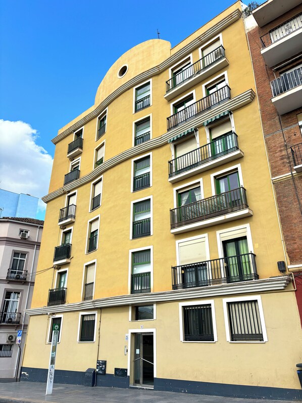 Un immeuble jaune à plusieurs étages, doté de balcons, d’une entrée au rez-de-chaussée et d’un numéro de porte bien visible.