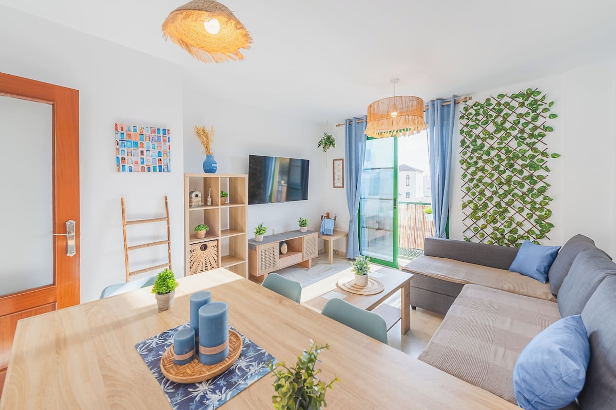 Een moderne woonkamer met een houten eettafel, een bank en een aan de muur bevestigde televisie.