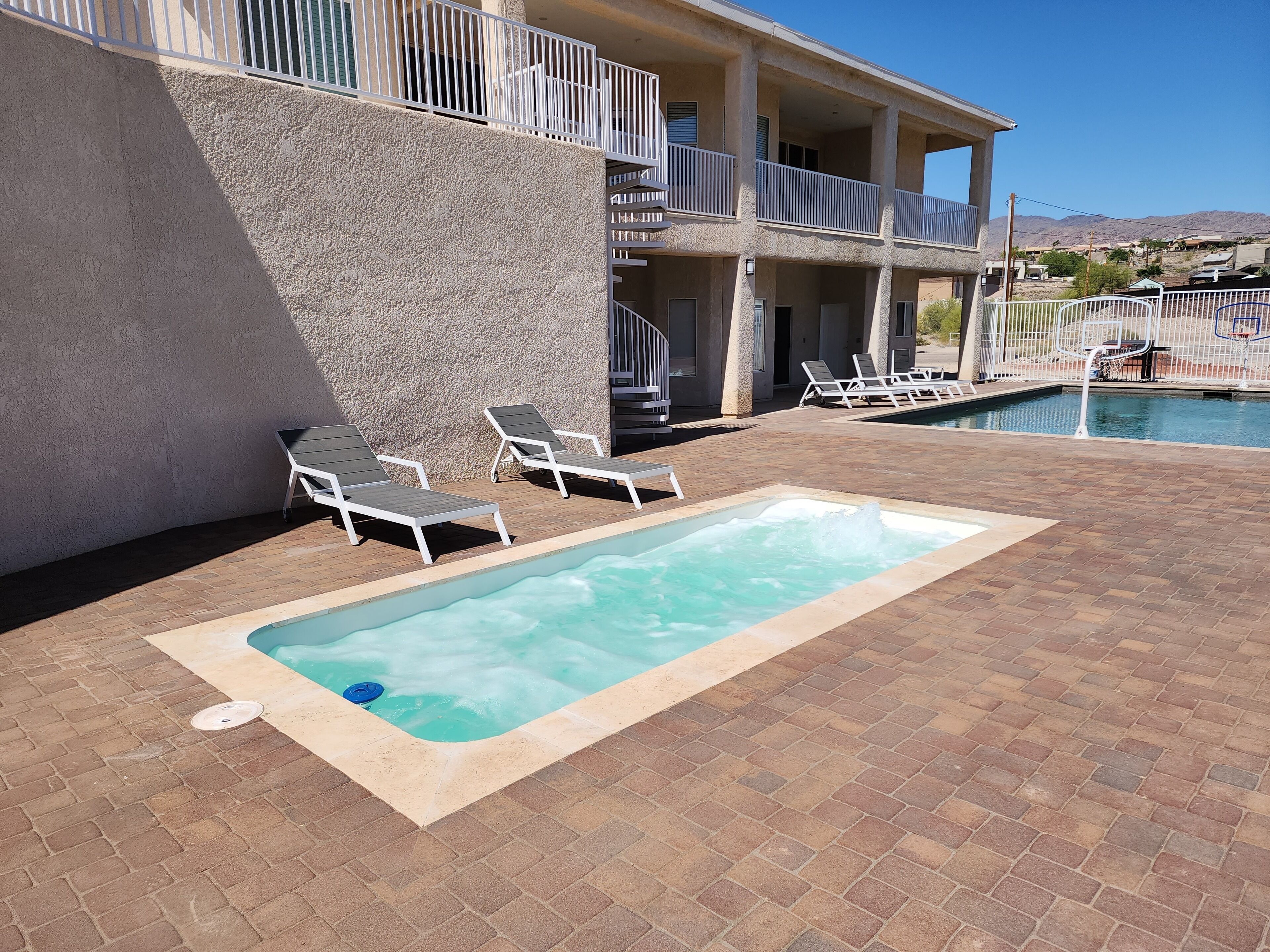 A pool area with lounge chairs, a hot tub, and a view of a mountain range.