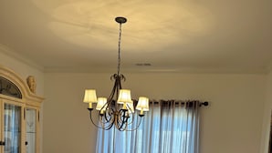 Uma sala de jantar com uma mesa de madeira, cadeiras, um lustre e um armário.