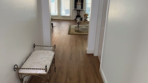 Um corredor com cama, piso de madeira e vista para uma sala de estar com mesa e vaso.