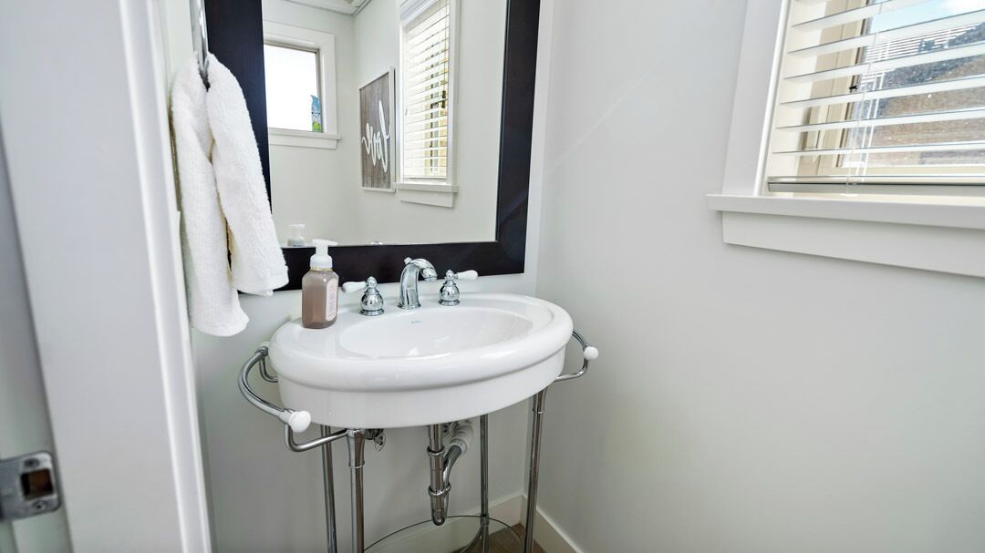 A bathroom with a white sink, a mirror, and a window with blinds.