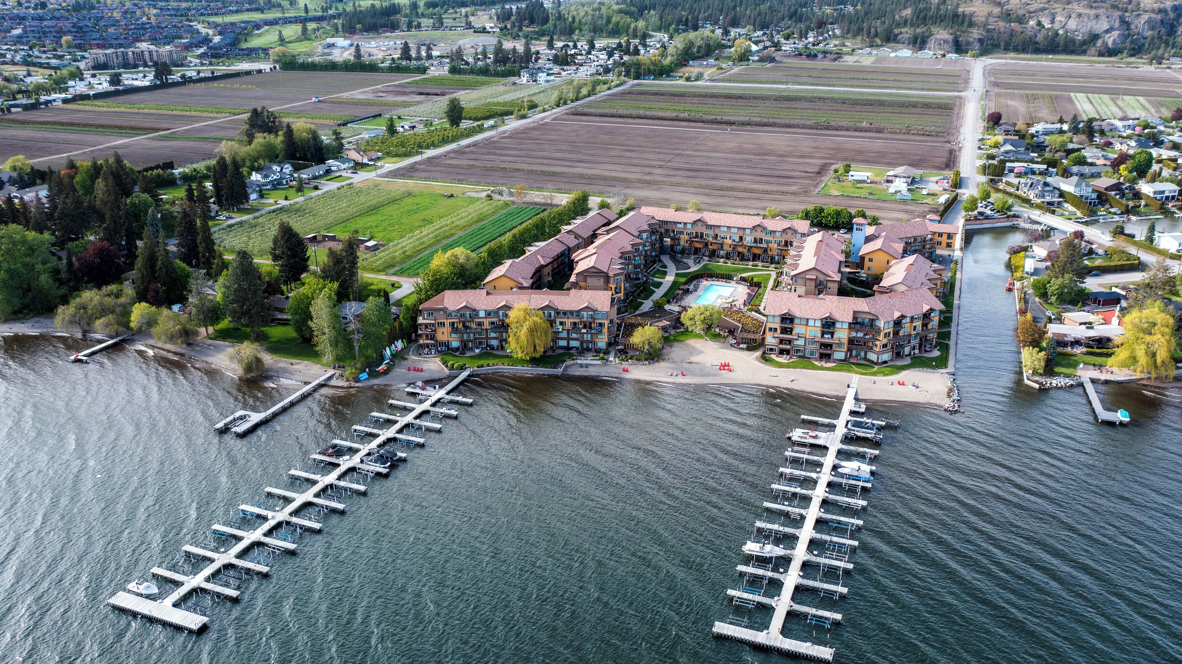 A waterfront hotel with multiple buildings, a marina with boats, and surrounding fields.