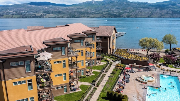 Un hôtel à plusieurs étages doté de balcons donnant sur un lac, d’une piscine et d’un jardin aménagé.