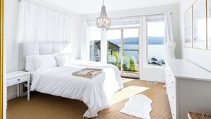 Une chambre dotée d’un grand lit, d’une table de chevet, d’une commode et offrant une vue sur un lac grâce à une porte-fenêtre coulissante.