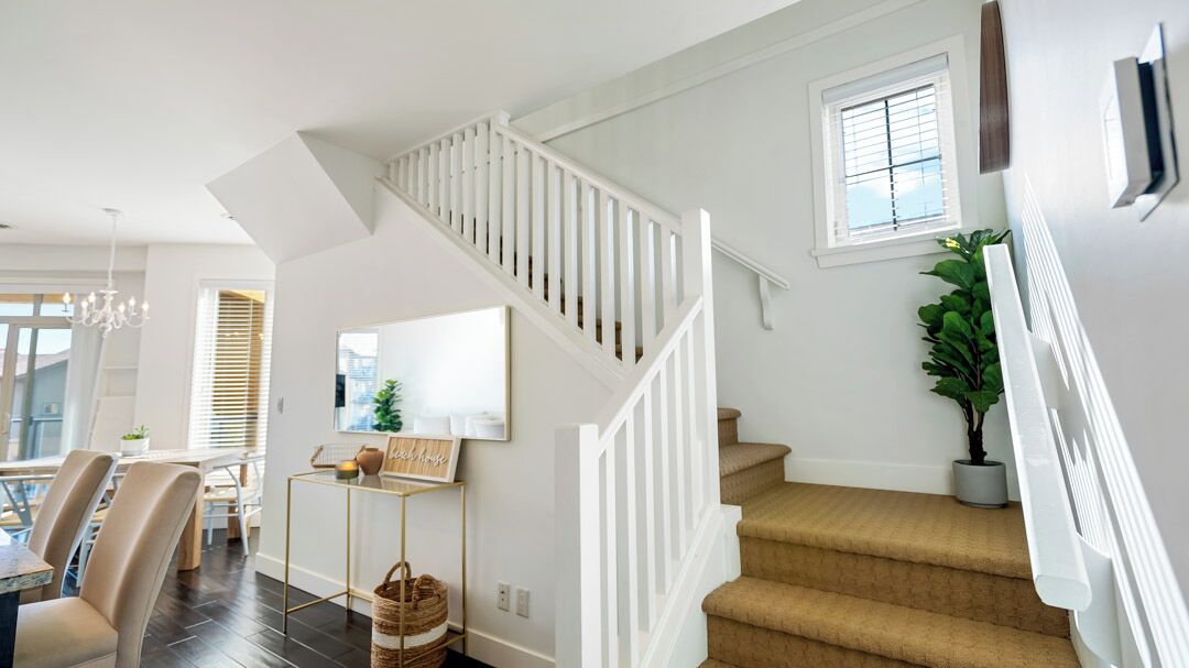 A modern interior with a staircase, a dining area with chairs and a table, and a potted plant.