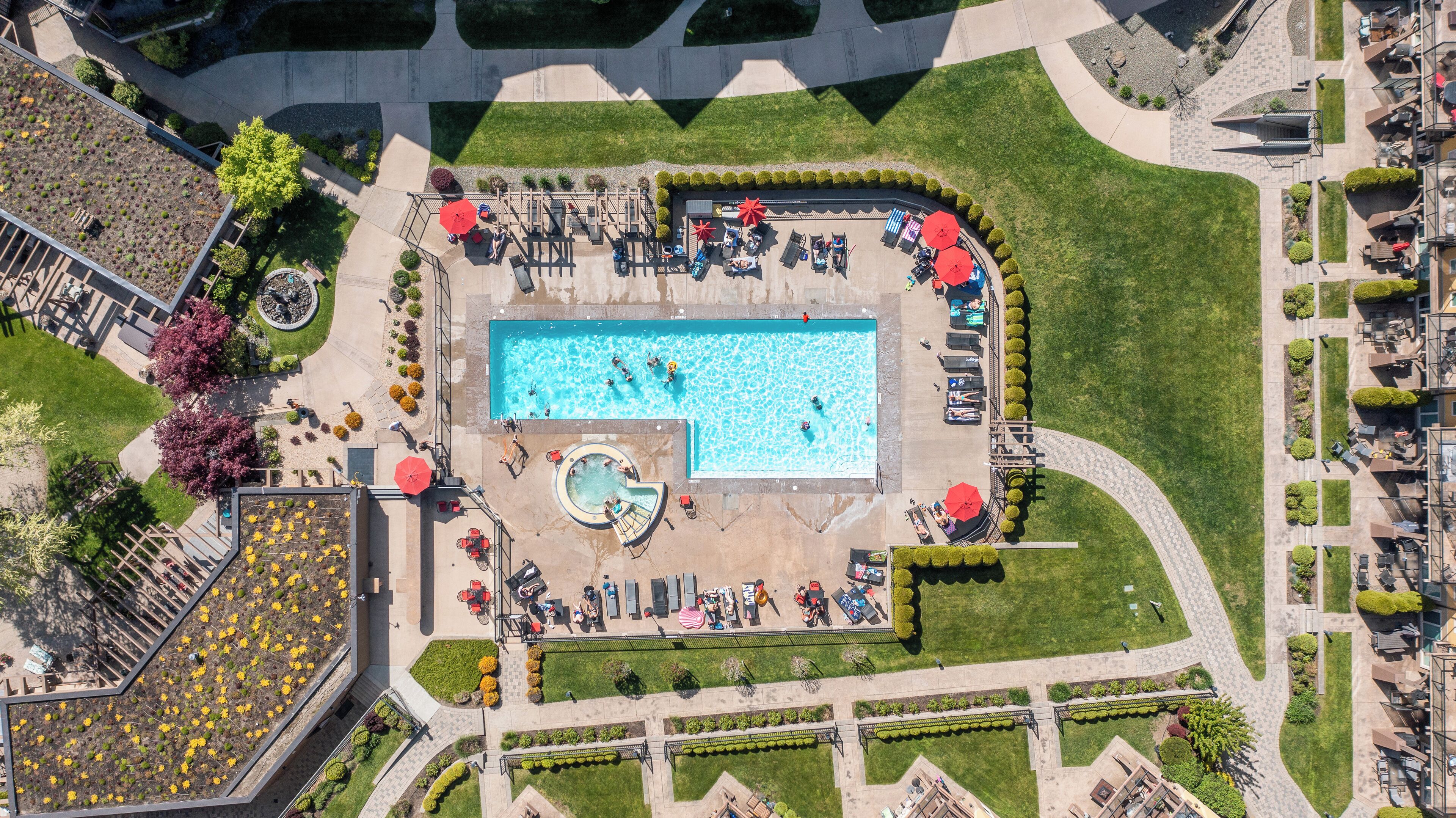 Vue aérienne d’un hôtel doté d’une piscine centrale, d’espaces de détente en plein air et de jardins aménagés.