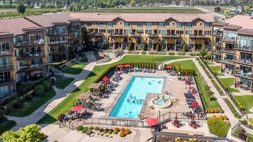 Un hotel de varios pisos con una piscina central rodeada de tumbonas y sombrillas, con un jardín ajardinado y vistas del entorno.