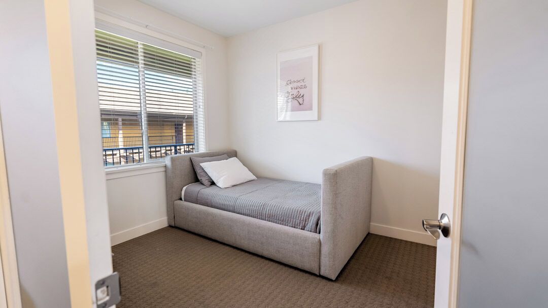 Una habitación pequeña y ordenada con un sofá cama gris, una ventana con persianas y un cuadro en la pared.