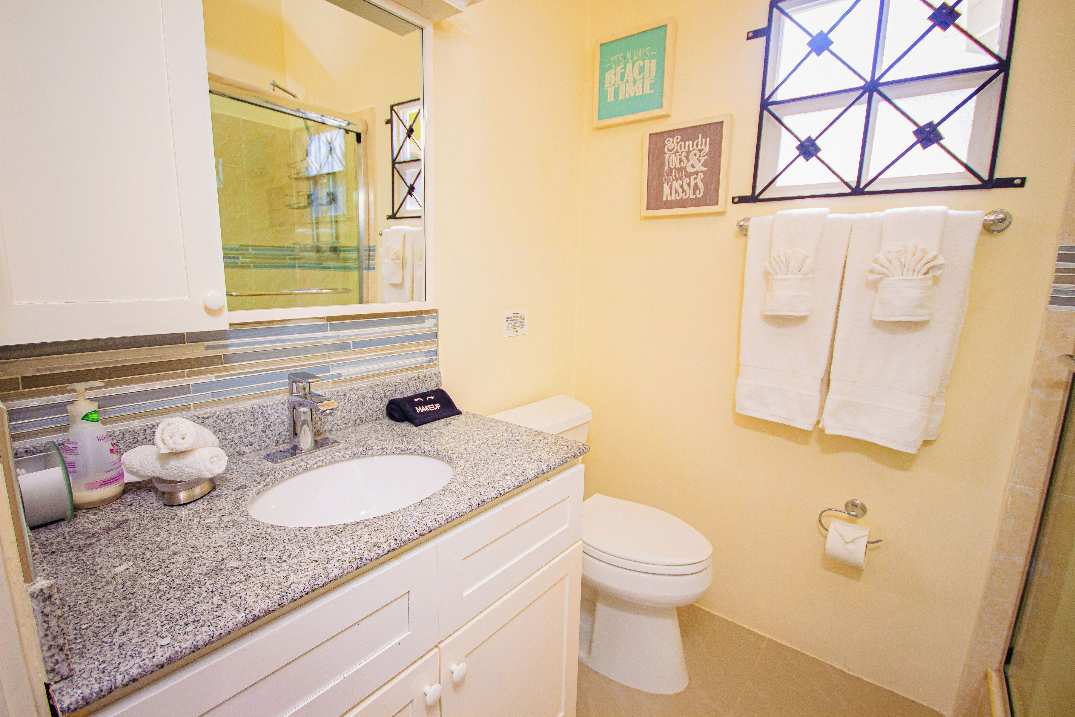 A bathroom with a sink, toilet, and glass shower enclosure. There are towels hanging on the wall and a framed picture.