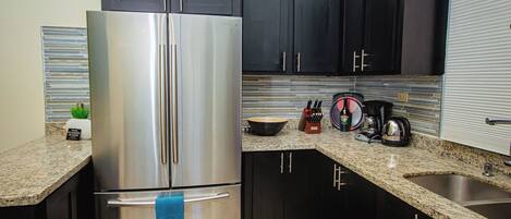 A kitchen with dark cabinets, a stainless steel refrigerator, granite countertops, and a sink.