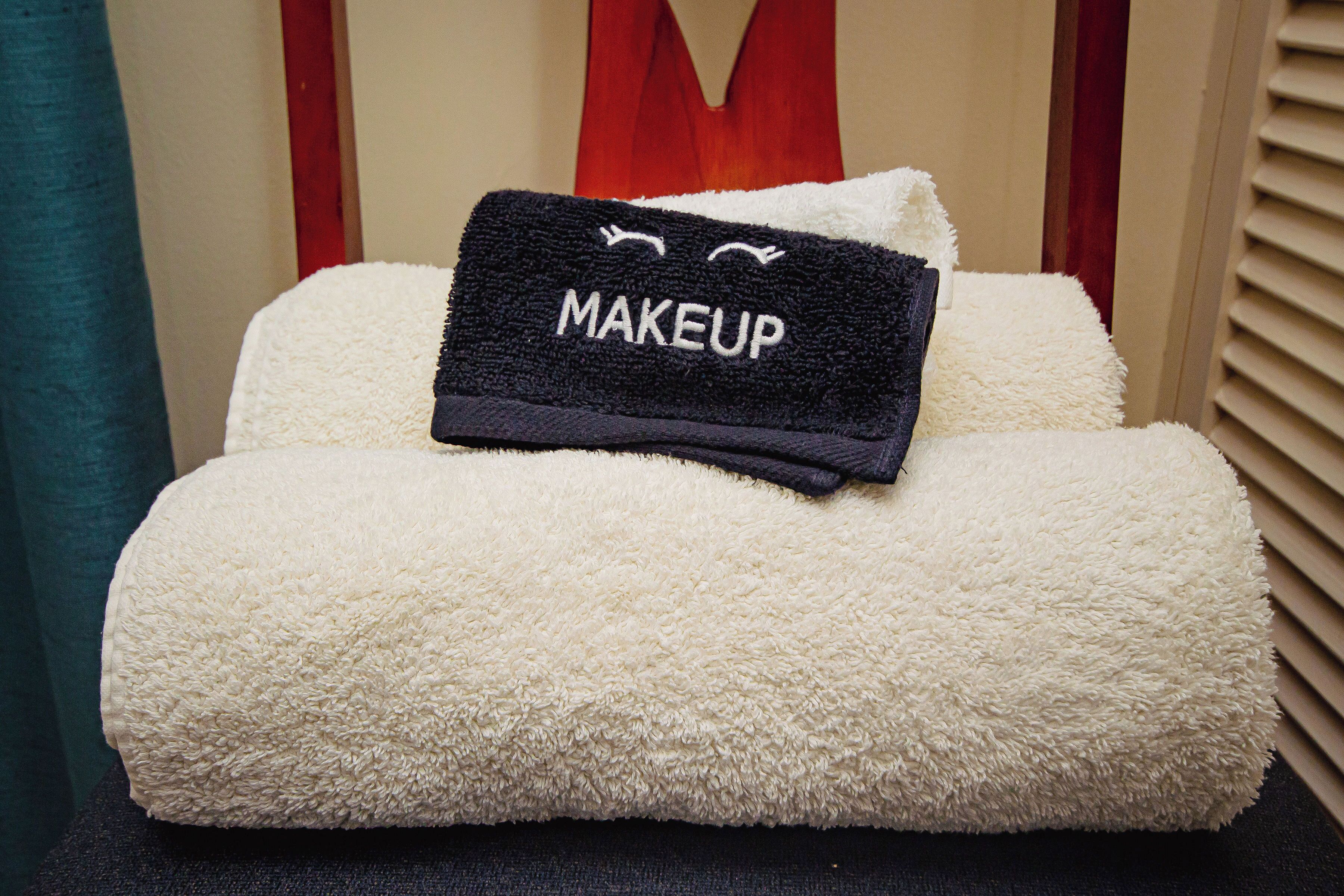 A neatly made bed with a fluffy white comforter and a black towel with 'MAKEUP' embroidered on it.