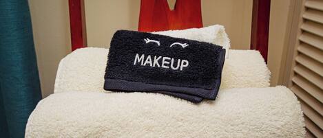 A neatly made bed with a fluffy white comforter and a black towel with 'MAKEUP' embroidered on it.