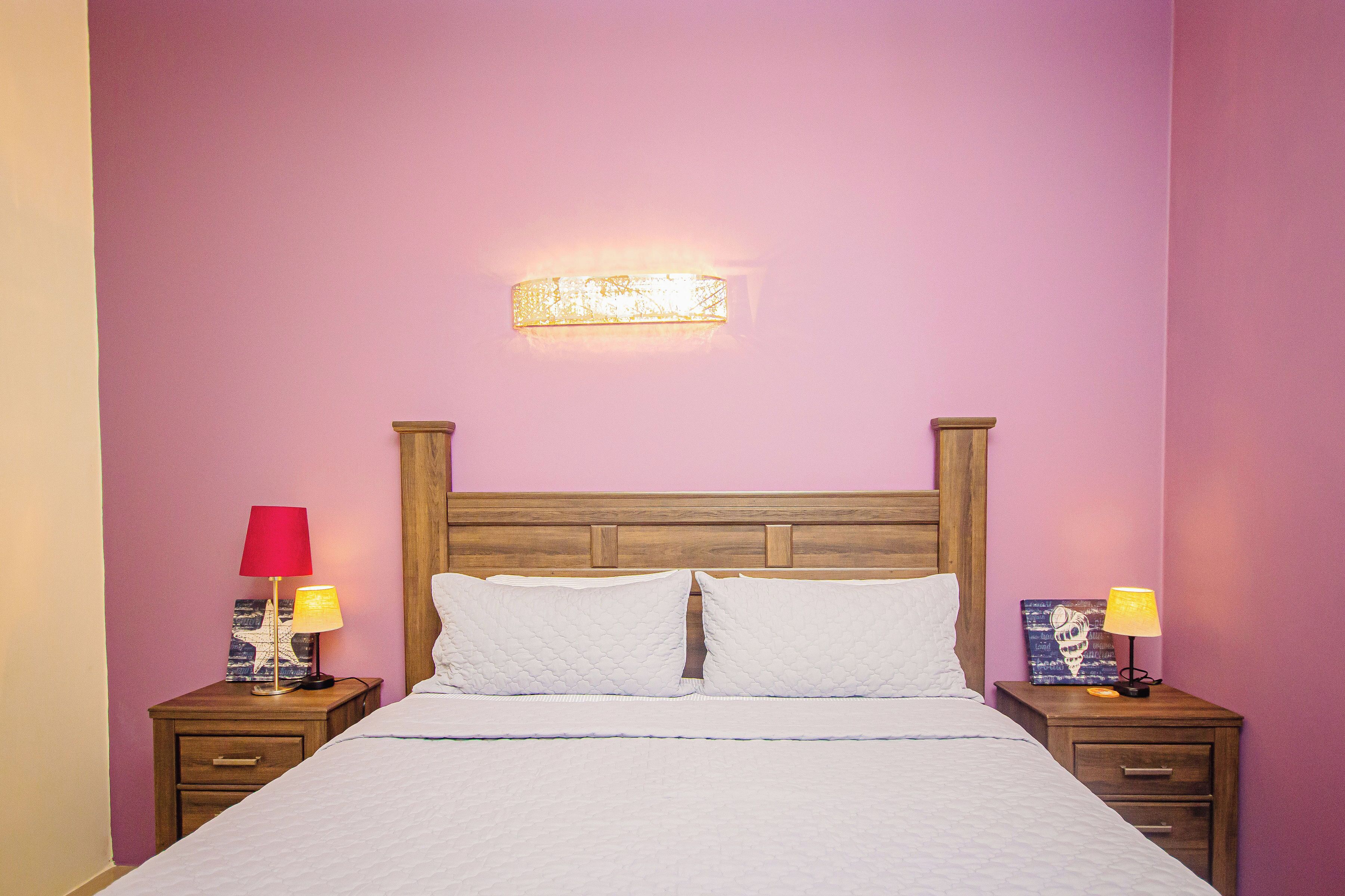 Una cama con ropa blanca, dos mesitas de noche con lámparas, y un aplique en la pared.