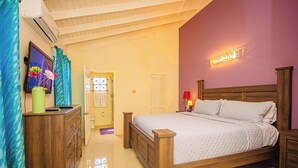 A bedroom with a wooden bed, a nightstand, a bedside table, a wall-mounted lamp, and a window with curtains. - Adorable Beach House In Draxhall (Ocho Rios)