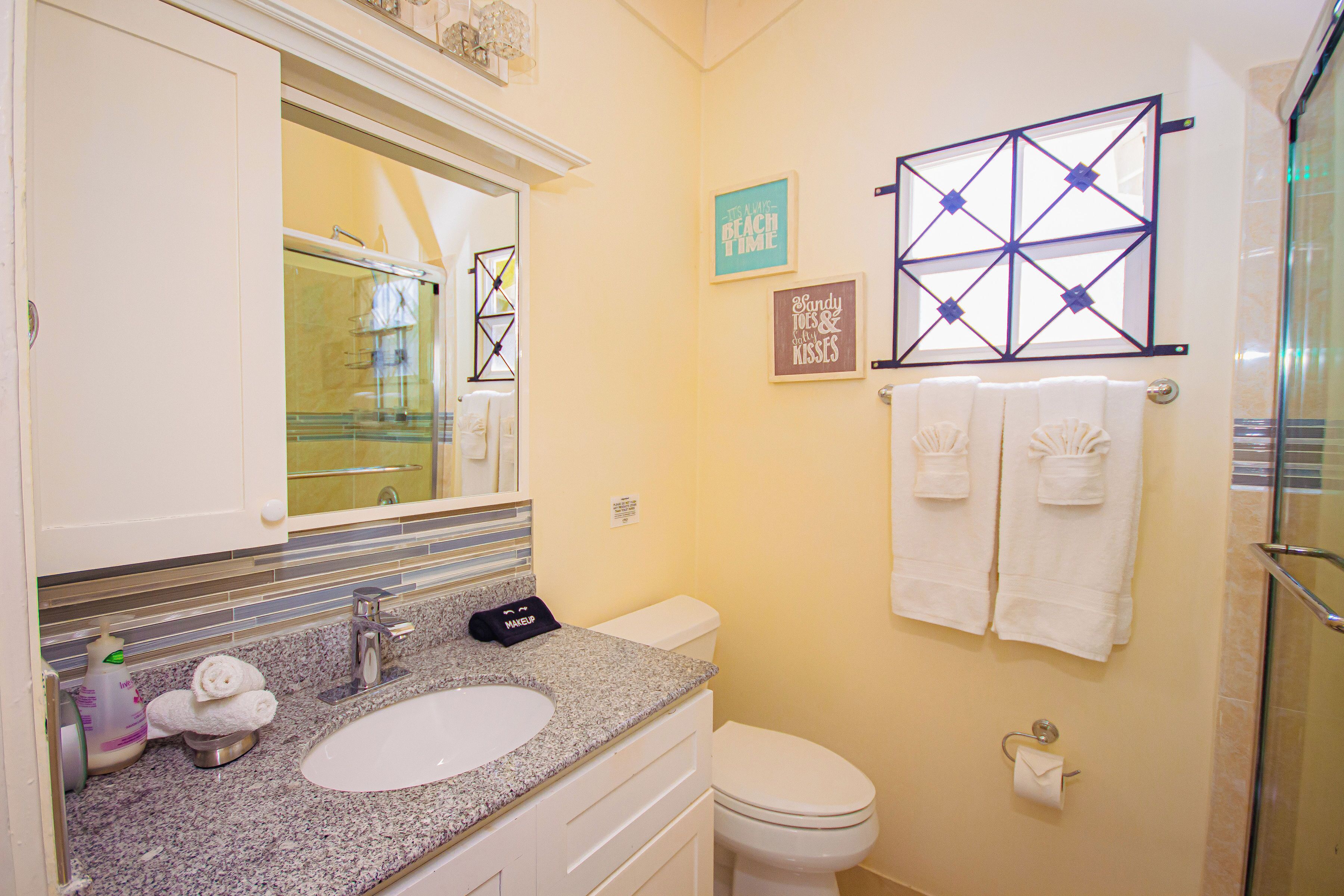Een badkamer met een wastafel met een granieten blad, een wit toilet en een douchecabine met glazen wanden.