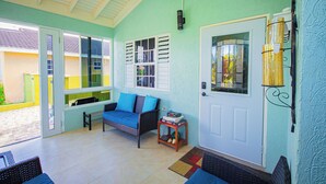 A room with a white door, a window with shutters, a bench, and a small table with books. - Adorable Beach House In Draxhall (Ocho Rios)