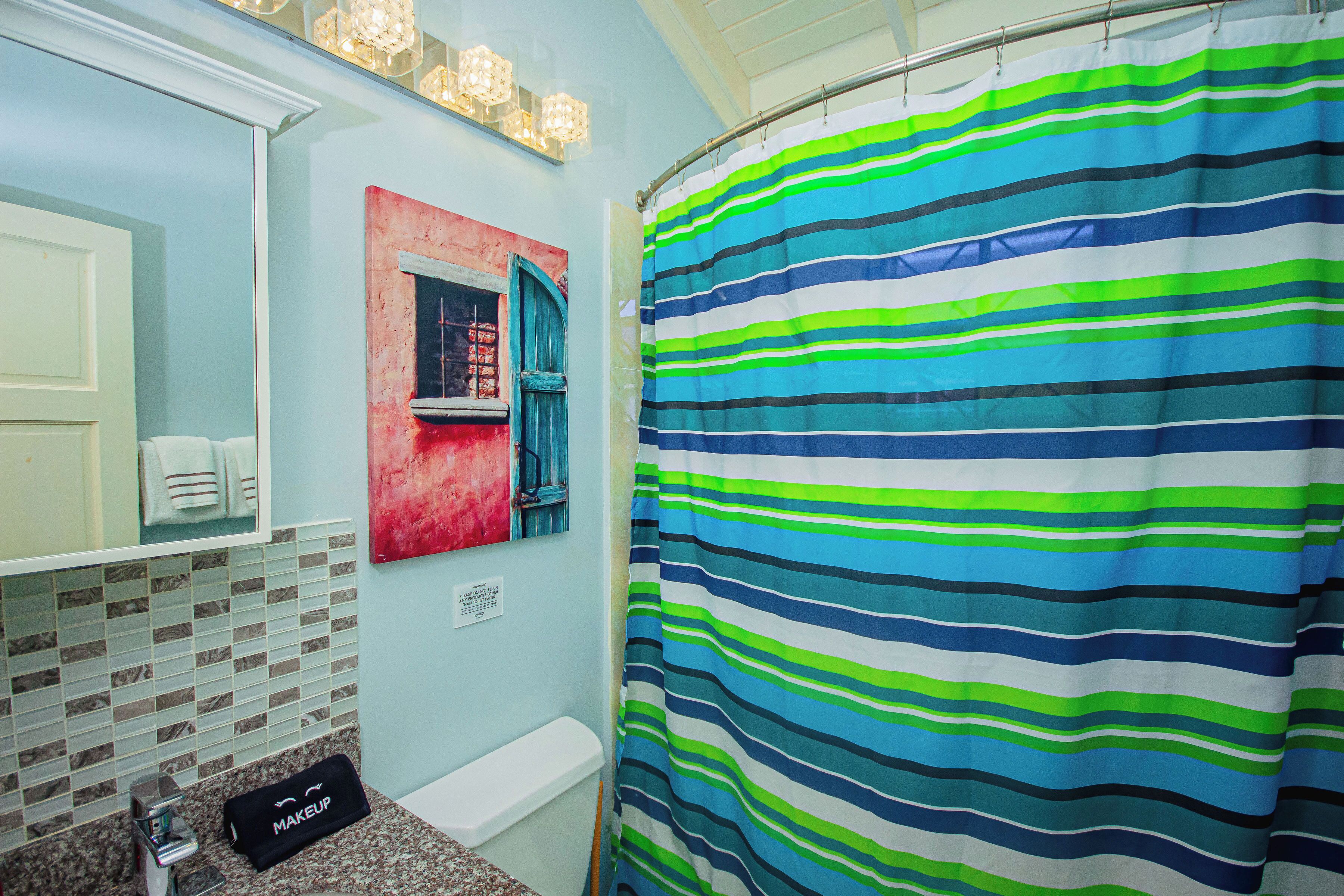 A bathroom with a striped shower curtain, a sink with a makeup bag, and a mirror with a red-framed window.