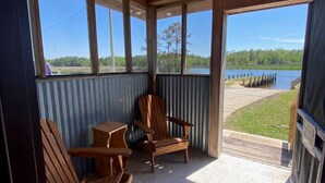 Overdkt terras met houten stoelen en een tafel, met uitzicht op een meer en een steiger.