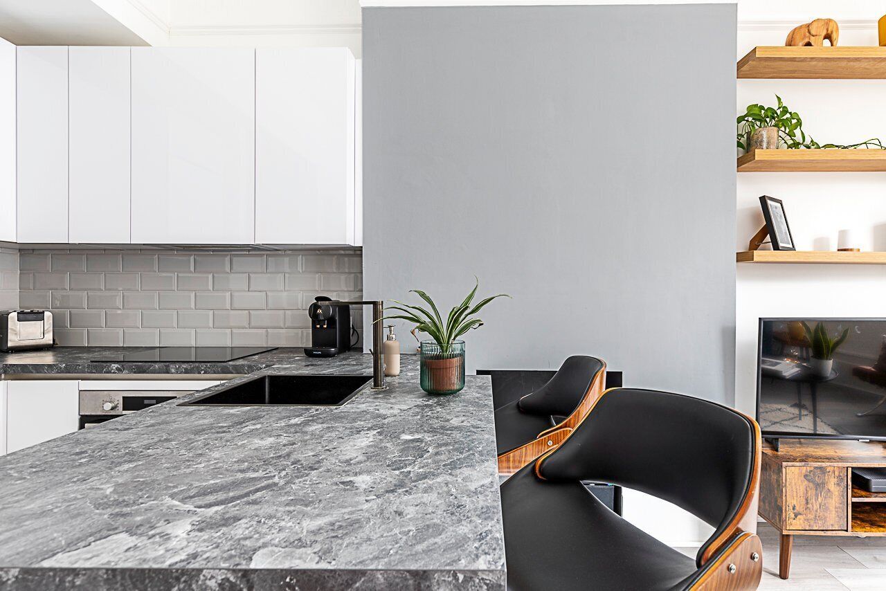 Une cuisine moderne avec des armoires blanches, un comptoir en marbre et une chaise noire.