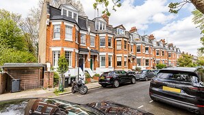 A row of terraced houses with a garage, parked cars, and a motorcycle on the street. - Stylish Hideaway Flat at Milton Park Highgate (London)