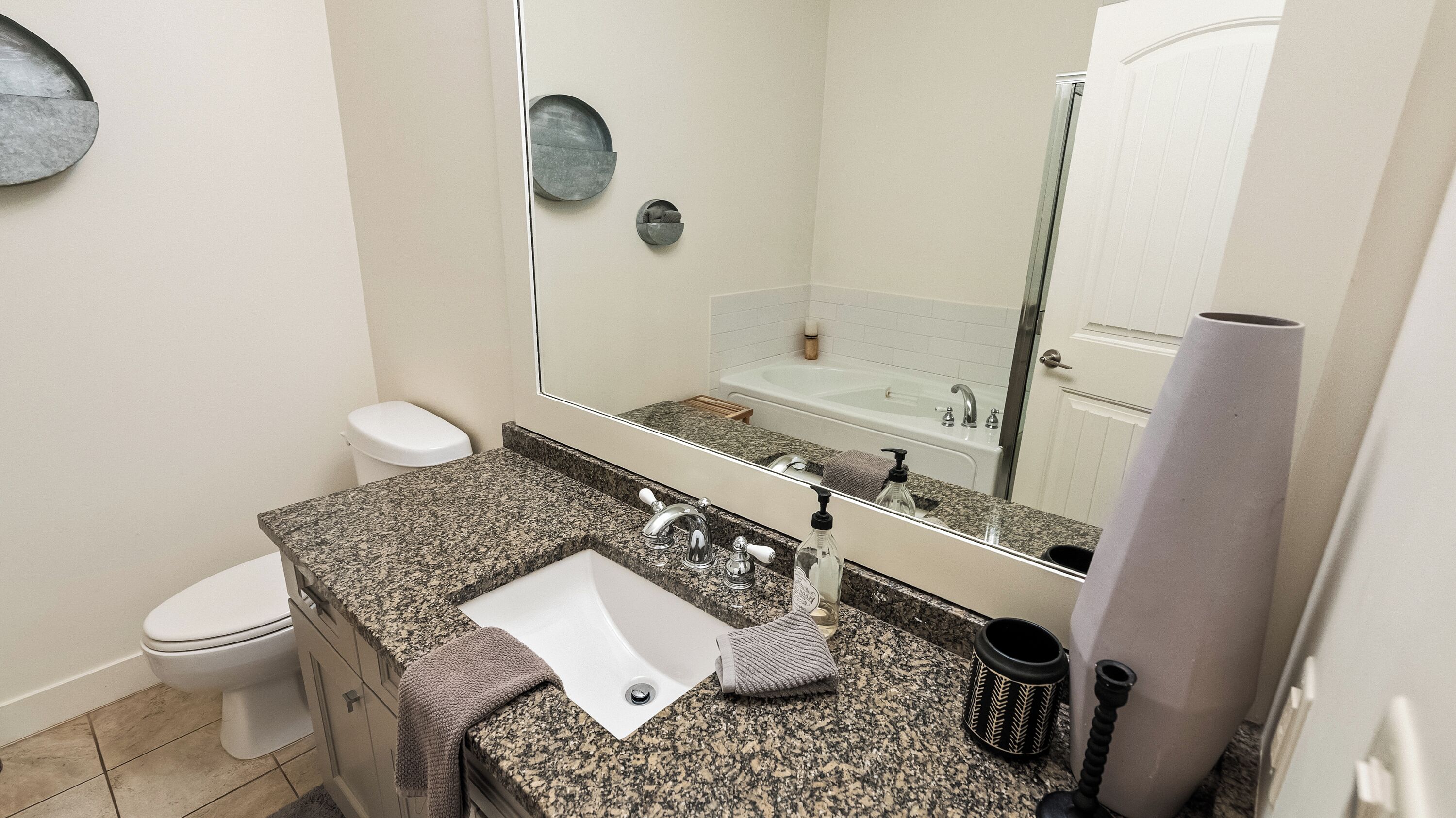 A bathroom with a granite countertop, a sink, a toilet, a bathtub, and a large mirror.