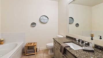 Un baño moderno con bañera, inodoro, tocador con lavabo y un espejo grande.
