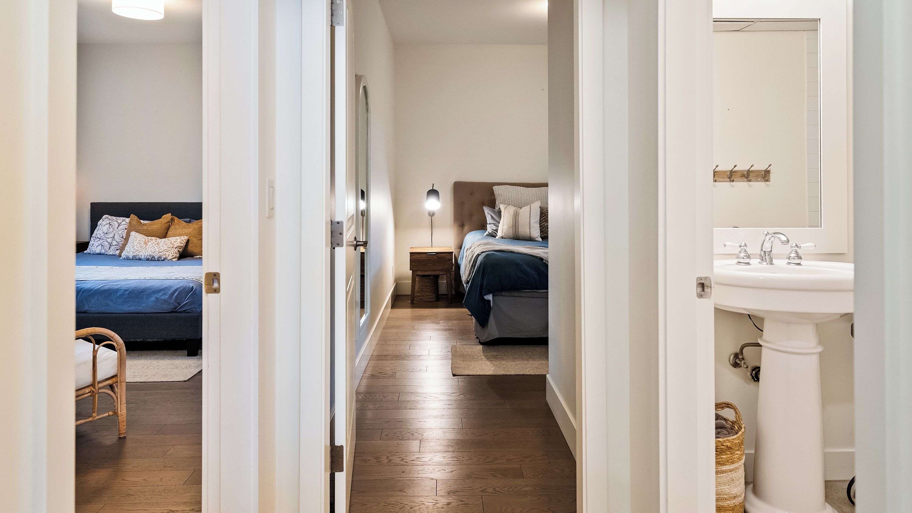 A narrow hallway leading to two bedrooms, each with a bed, bedside table, and lamp. A bathroom with a sink and mirror is visible to the right.