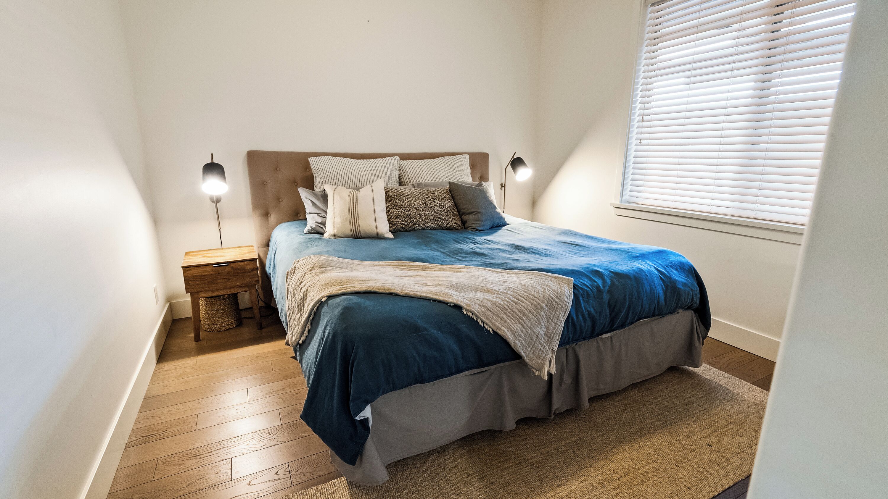 A bedroom with a bed, nightstand, lamp, and a window with blinds.