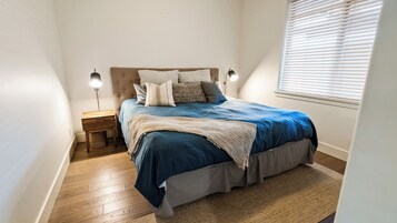 Un dormitorio con cama, mesita de noche, lámpara y ventana con persianas.