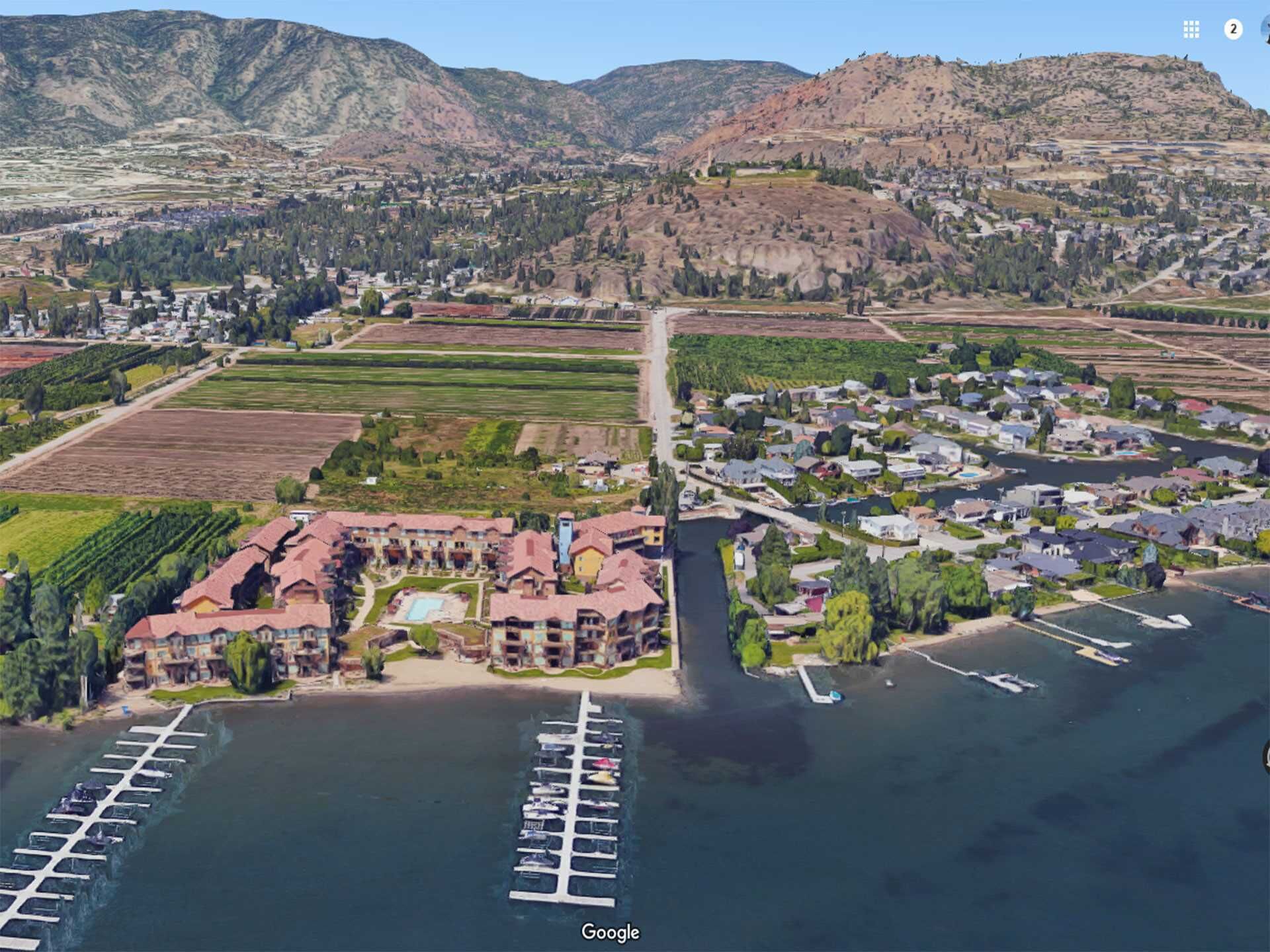 An aerial view of a coastal town with a marina, residential areas, and agricultural fields.