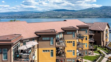 A multi-story hotel with balconies, a pool area, and a view of a lake and mountains.