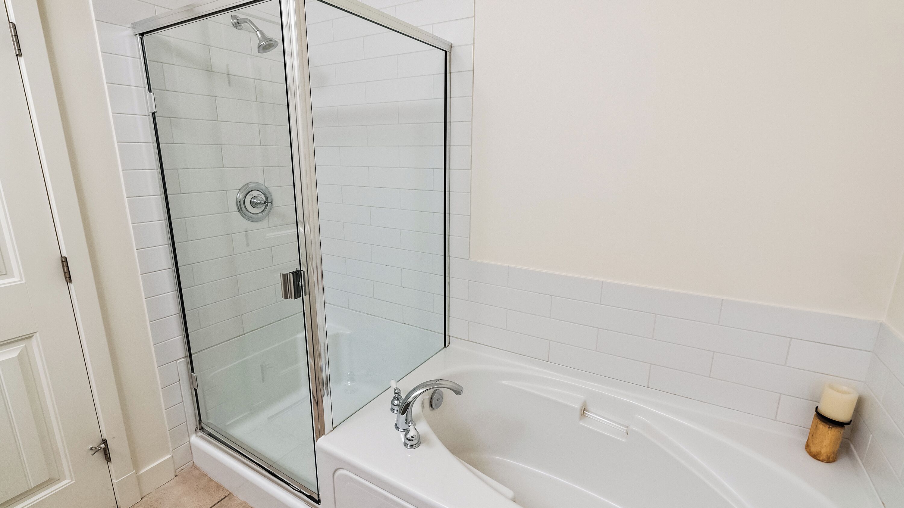 A modern bathroom with a glass-enclosed shower, a white bathtub, and a small candle on the side.