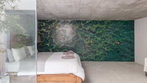 A bedroom with a bed, a green wall mural, and a glass partition.