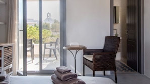 A hotel room with a bed, a chair, a small table, and a view of a building with a bell tower.