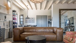 A spacious living room with a large leather sofa, a round coffee table, and two armchairs. A dining area with a table and chairs is visible in the background.