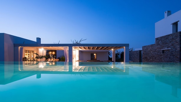 A modern house with a swimming pool, a covered patio, and a stone wall.